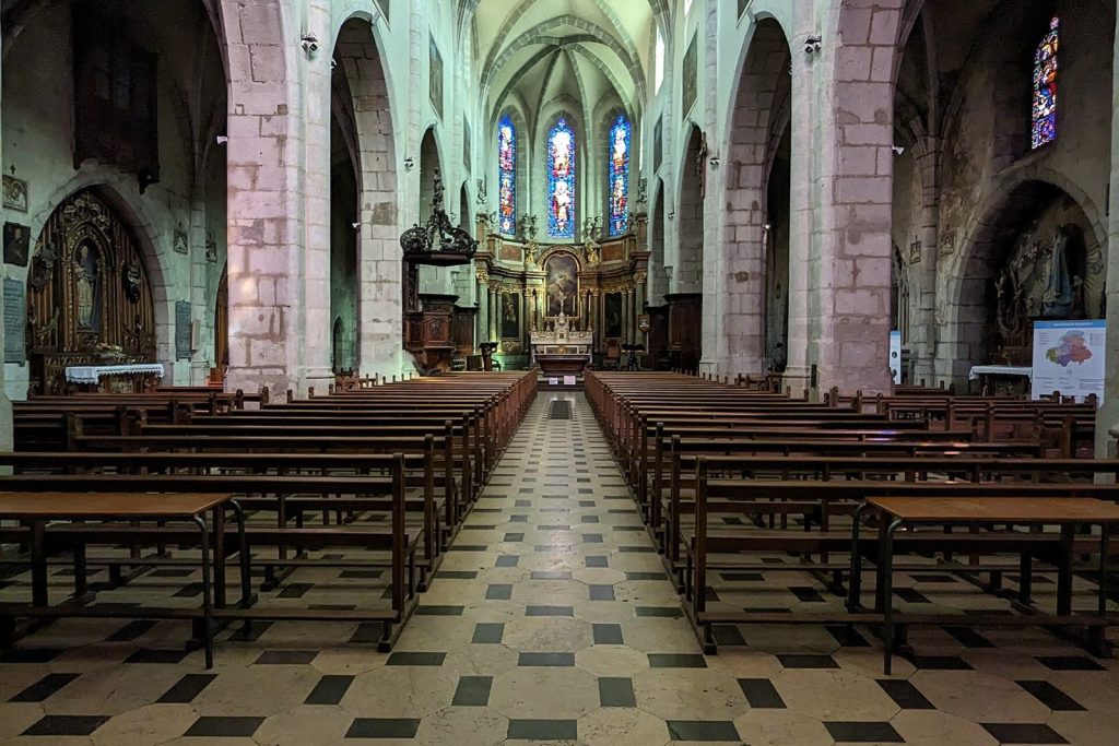 Nef gothique de la cathédrale Saint-Pierre d'Annecy vue depuis le portail, avec la chaire et le chœur éclairé