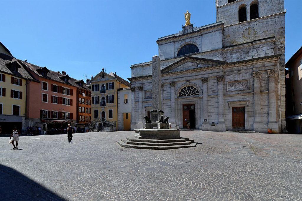 Façade néoclassique de l'église Notre-Dame-de-Liesse, son clocher médiéval et la fontaine à obélisque de la place Notre-Dame à Annecy