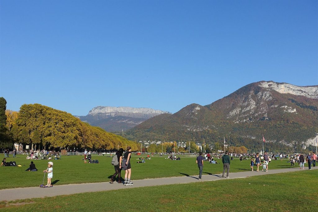 Pelouse du Pâquier au bord du lac d'Annecy, promeneurs et montagnes en automne