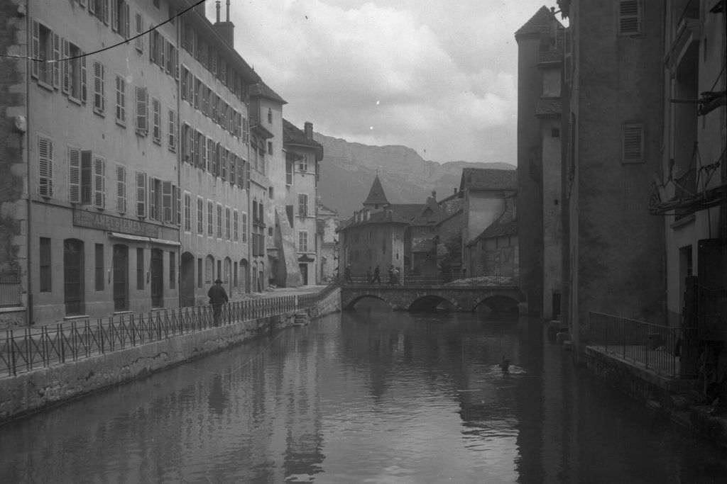 Le Thiou et ses quais dans la Vieille Ville d'Annecy vers 1926, avec un pont de pierre et le Palais de l'Isle