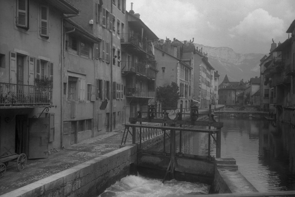 Une vanne sur le Thiou dans la Vieille Ville d'Annecy vers 1926, maisons à balcons et Palais de l'Isle au fond