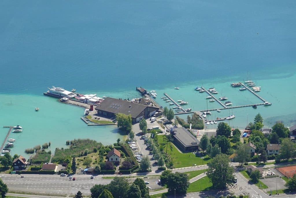 Le port de Sevrier vu d'en haut : l'eau turquoise des hauts-fonds, puis le bleu profond du lac
